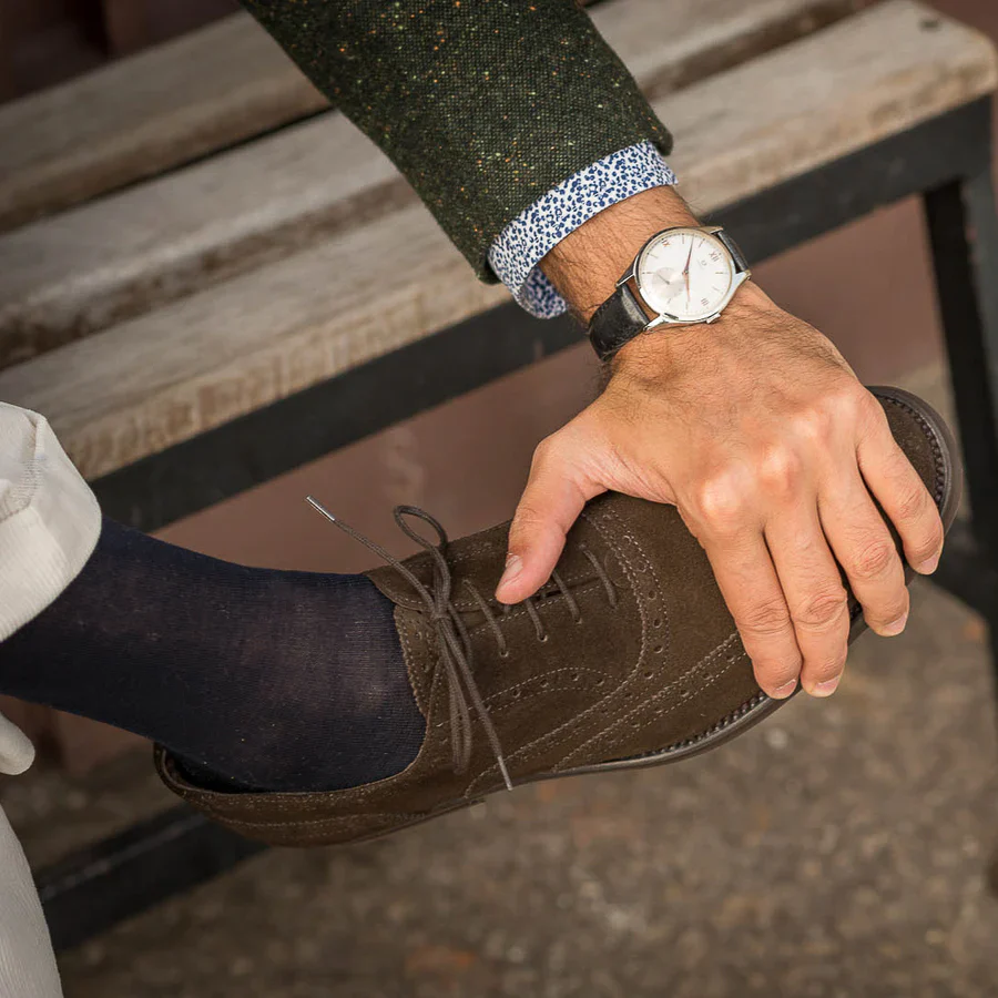 A person sits with their hand on their brown suede shoe