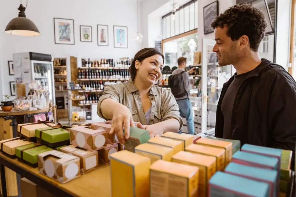 Smiling female owner talking to male customer while working in shop