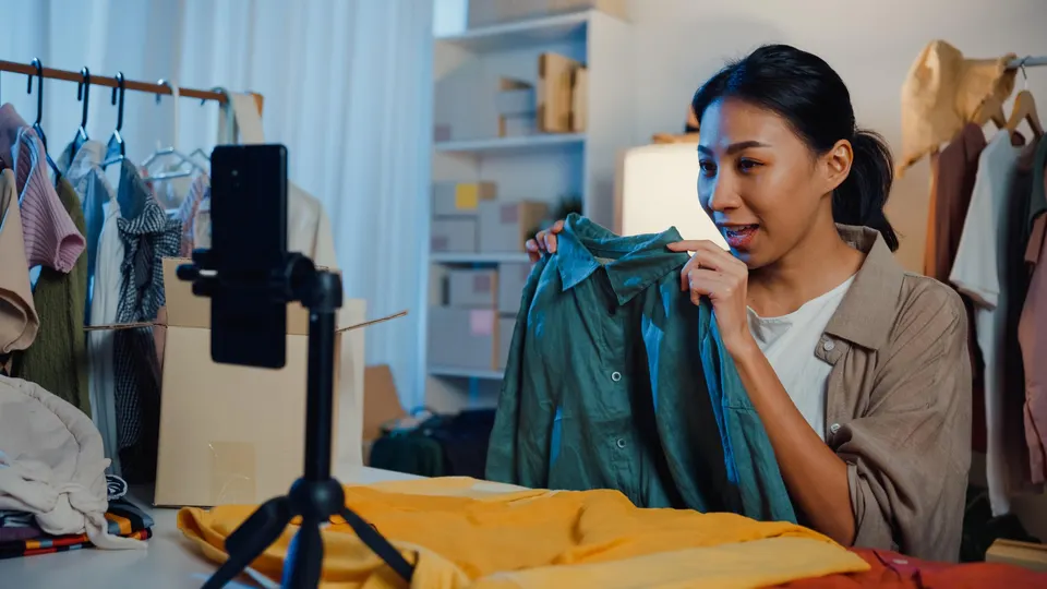 Asian businesswoman live-streamed ecommerce sell clothes in home at night. Beautiful girl using the smartphone and tablet for recording video.