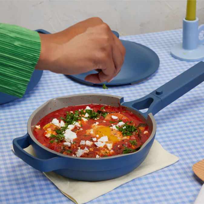 A person sprinkles something into a blue pan atop a blue gingham tablecloth