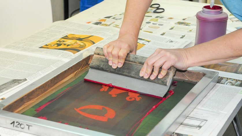 Screenprinting using a squeegee to transfer paint onto material through a perforated screen.