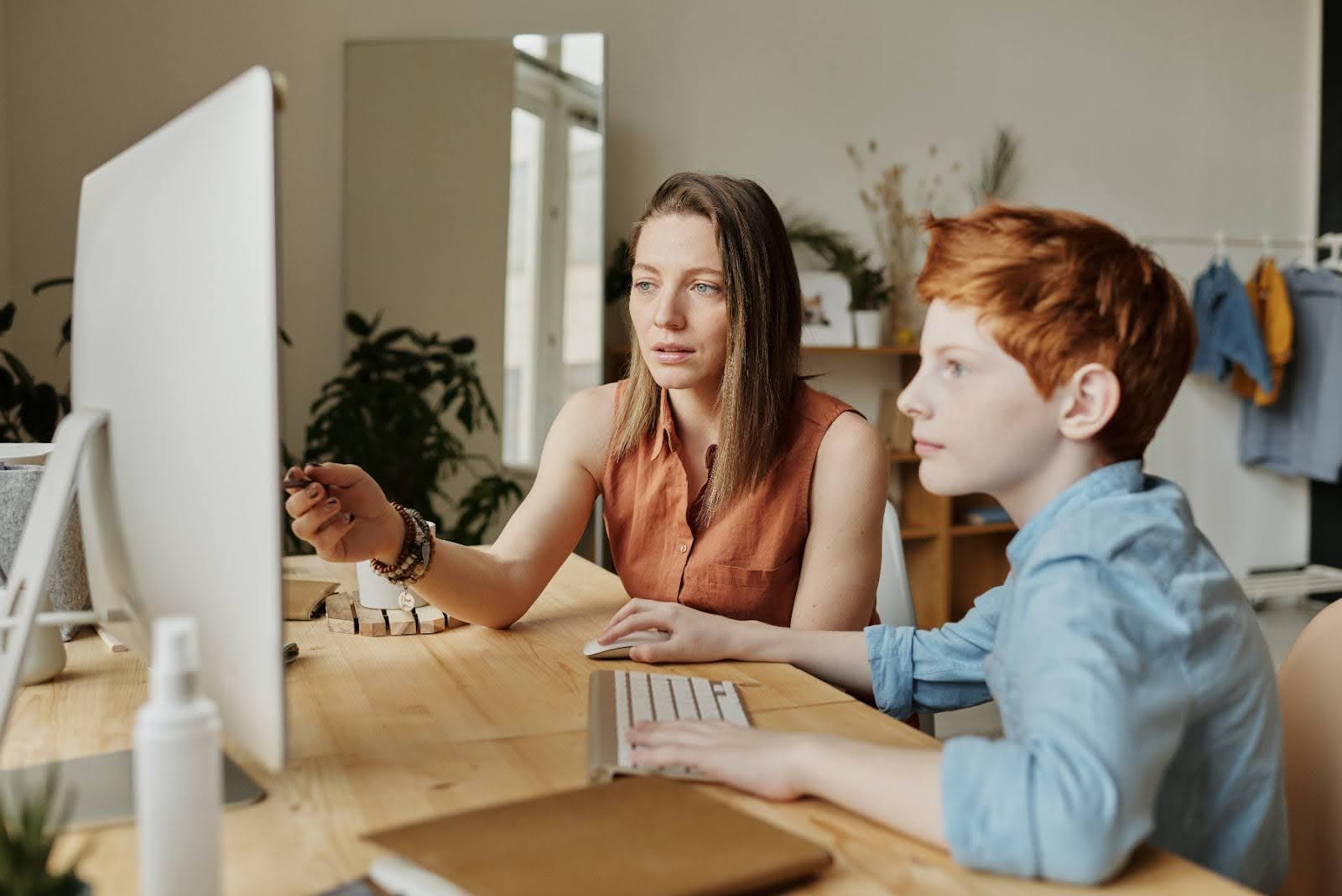 A parent helps her child work on a project on a computer.