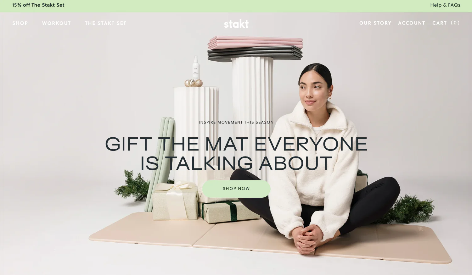 Stakt yoga mat homepage with a model in cozy attire sitting on a foldable mat surrounded by gifts.