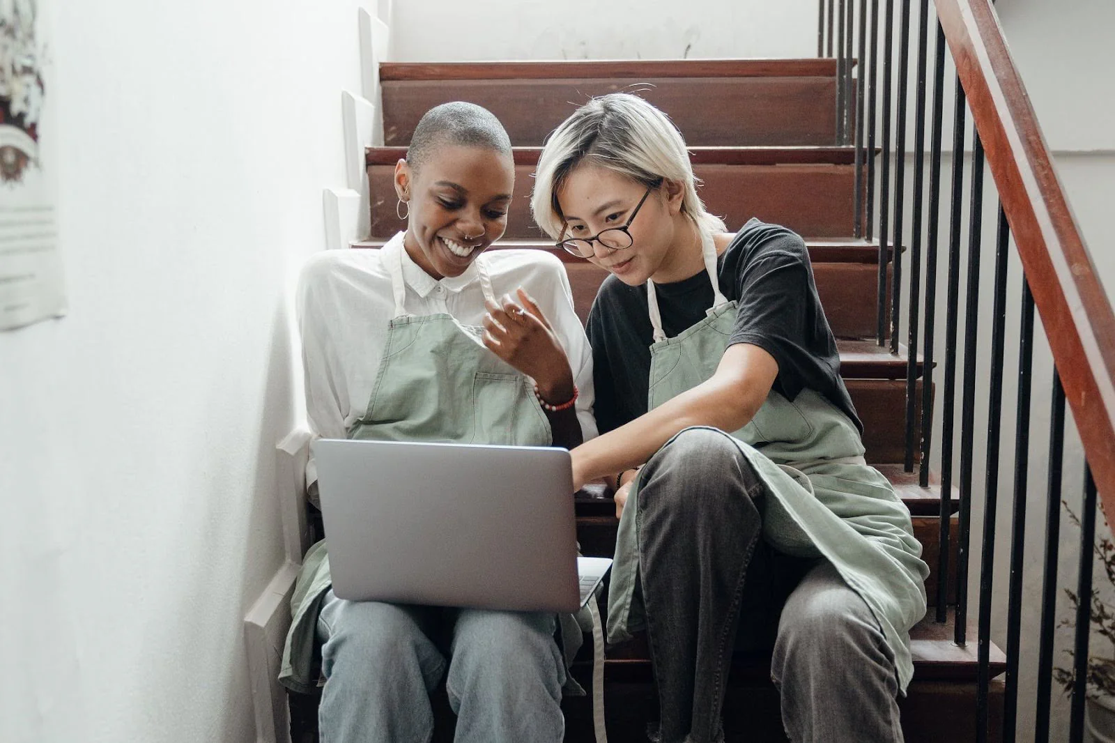Two students sit on a stair looking at a laptop.