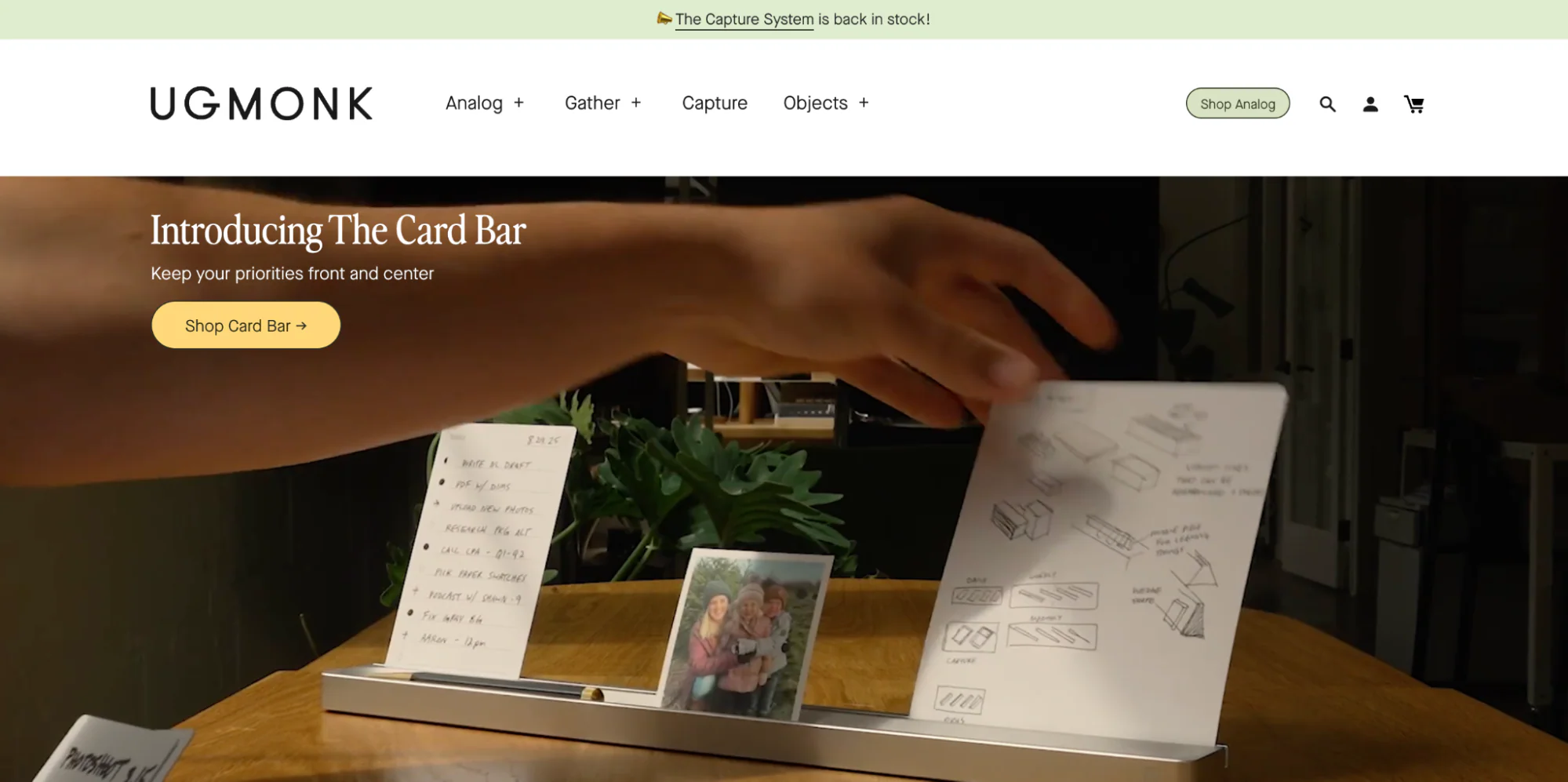 Ugmonk’s homepage with a yellow button on top of a photo of someone arranging cards.