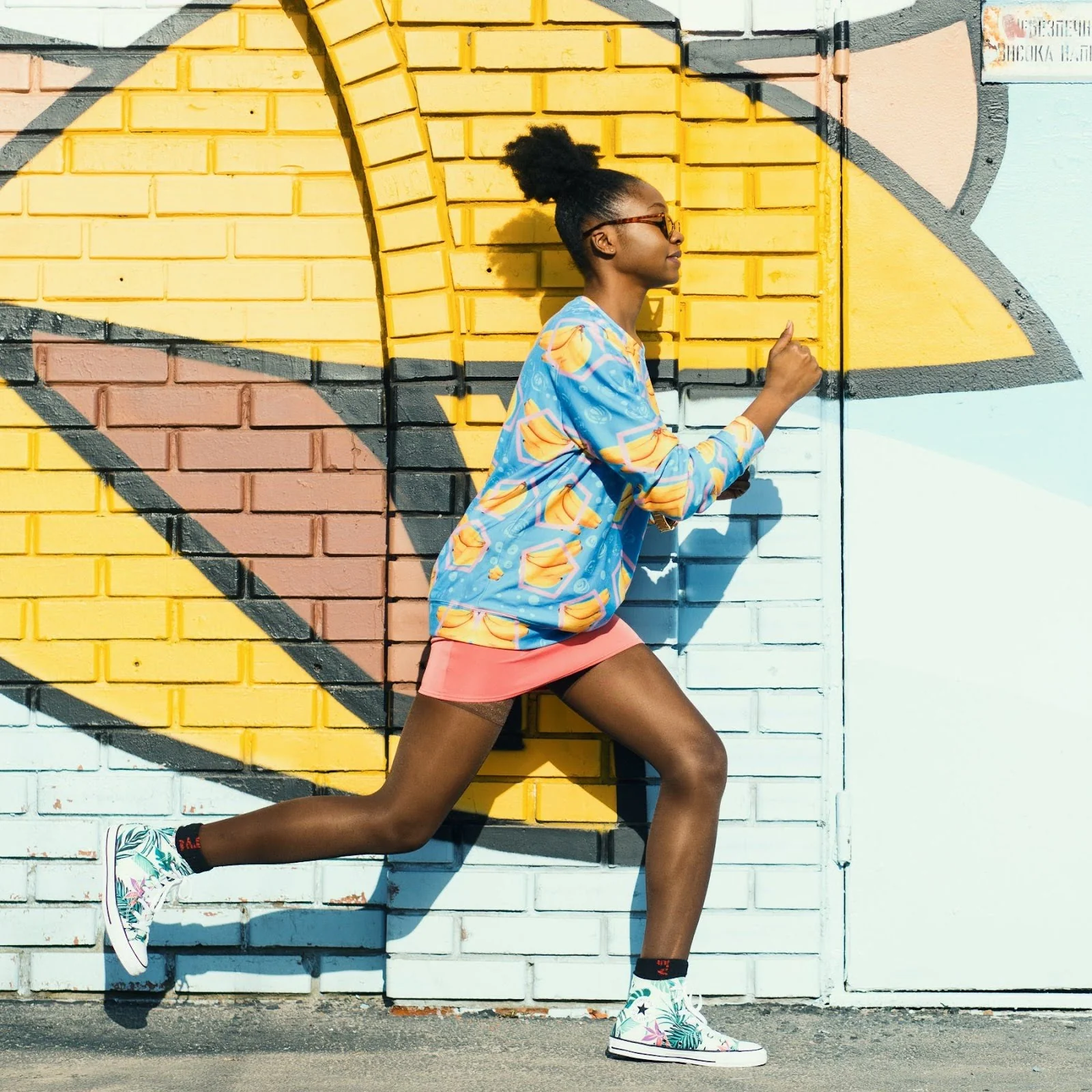 A young woman runs in front of a painted brick wall.
