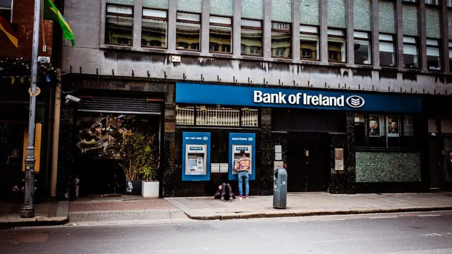 Person using an ATM outside a Bank of Ireland branch on a city street during daytime.