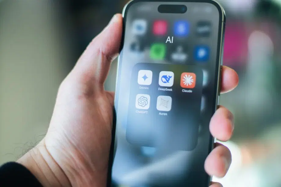 A hand holds a smartphone displaying an AI folder with five artificial intelligence app icons on the screen.