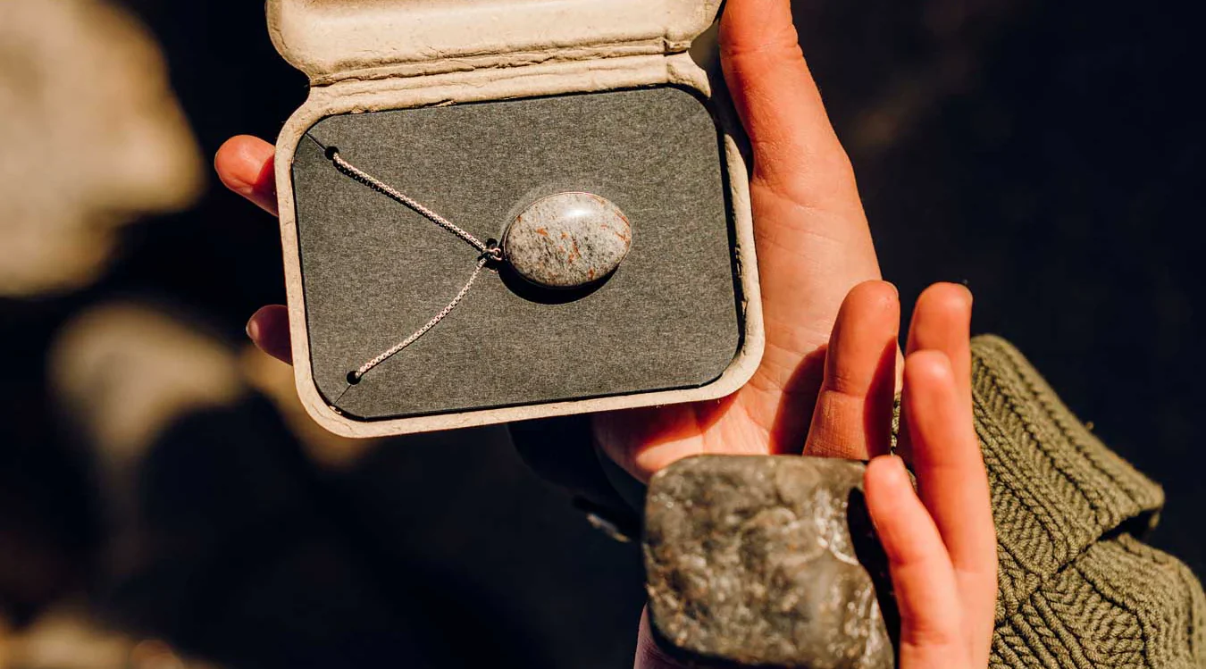 An open box showing a gray, oval stone necklace.
