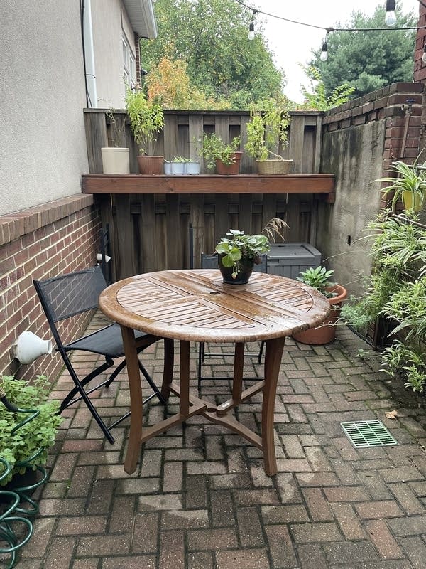 A small, round brown table in a fenced in outdoor area with brick flooring.
