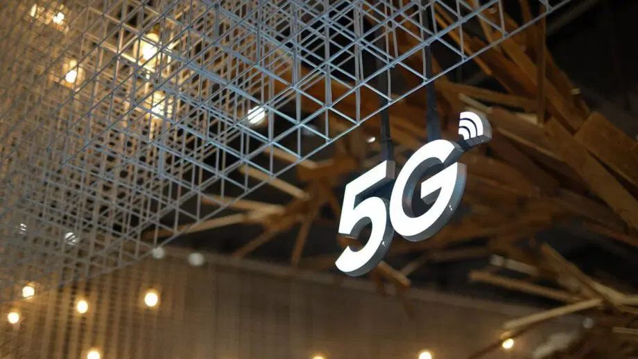 A glowing 5G sign hangs under a metal grid structure with small lights blurred in the background.
