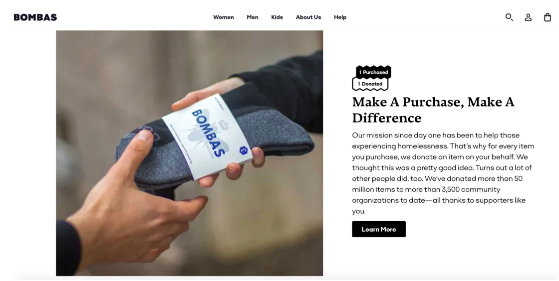 Bombas’ promotional image; a close-up of a hand giving a pair of Bombas socks to another hand. To the left, is a description of Bombas's practice of giving a free pair of socks for every pair sold. The headline reads, "Make a Purchase, Make a Difference."