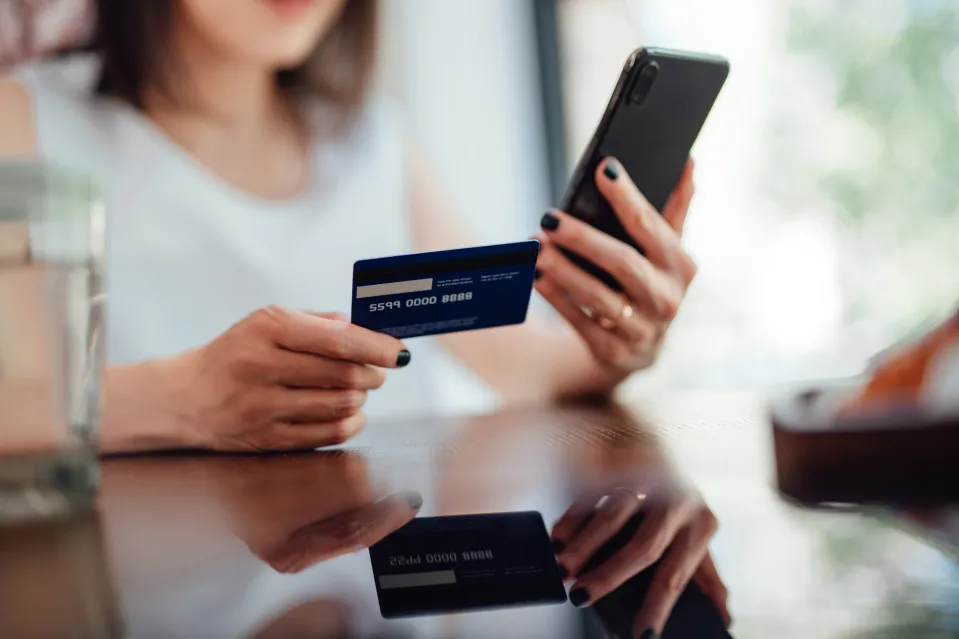A person holds a credit card and a smartphone, preparing to make an online purchase.
