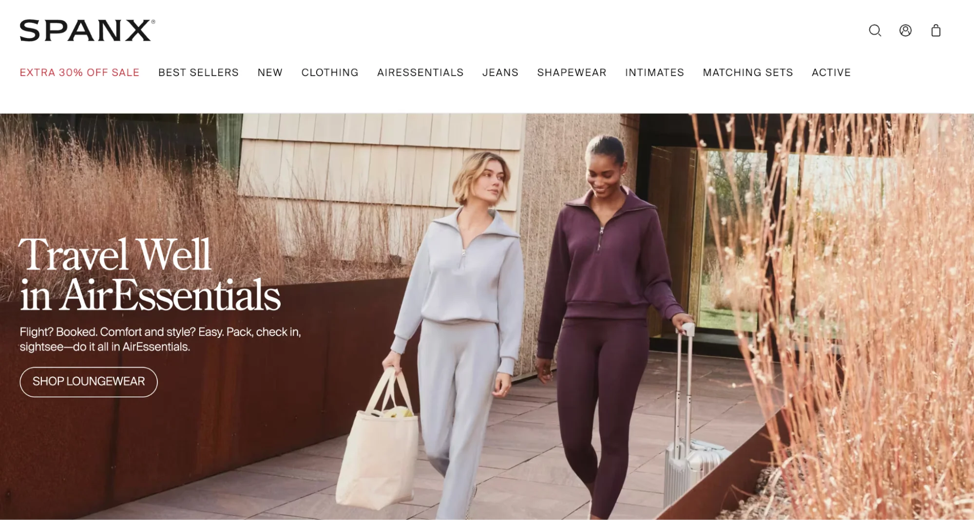 Two women walking with luggage in loungewear for the Spanx AirEssentials ad.