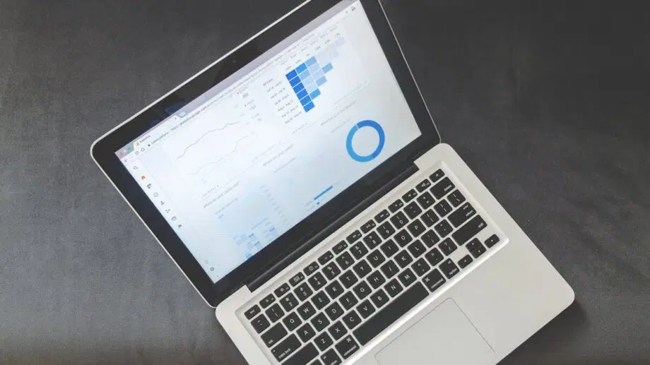 Open laptop displaying data charts and graphs on the screen, placed on a dark surface with a wooden floor visible.