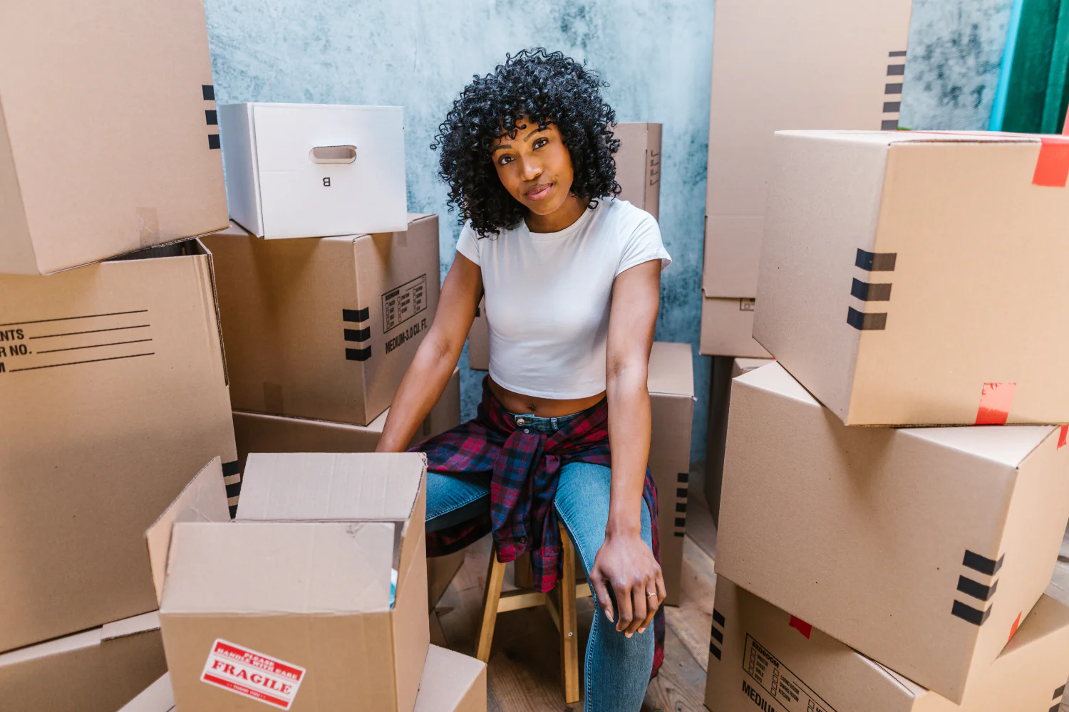 Person sits among a pile of cardboard shipping boxes looking at the camera