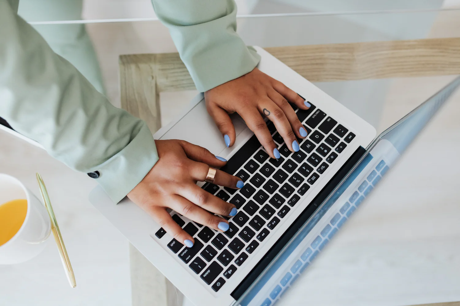 Person with painted nails with a gold ring on types on a laptop